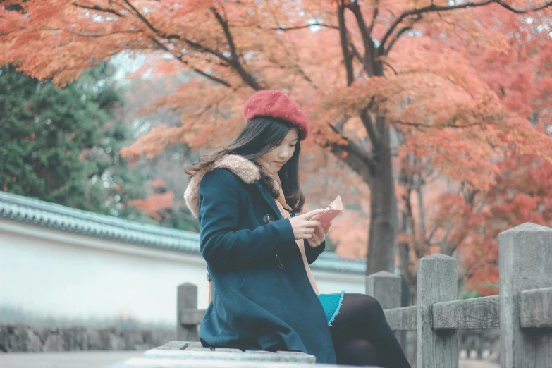 a woman sitting on a bench looking at her cell phone, inspired by Itō Shinsui, pexels contest winner, autumn color, nezuko, wearing teal beanie, japan sightseeing