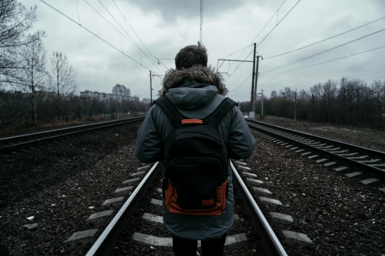 a person on a train track with a backpack, pexels contest winner, realism, gray skies, standing upright, back facing, male teenager