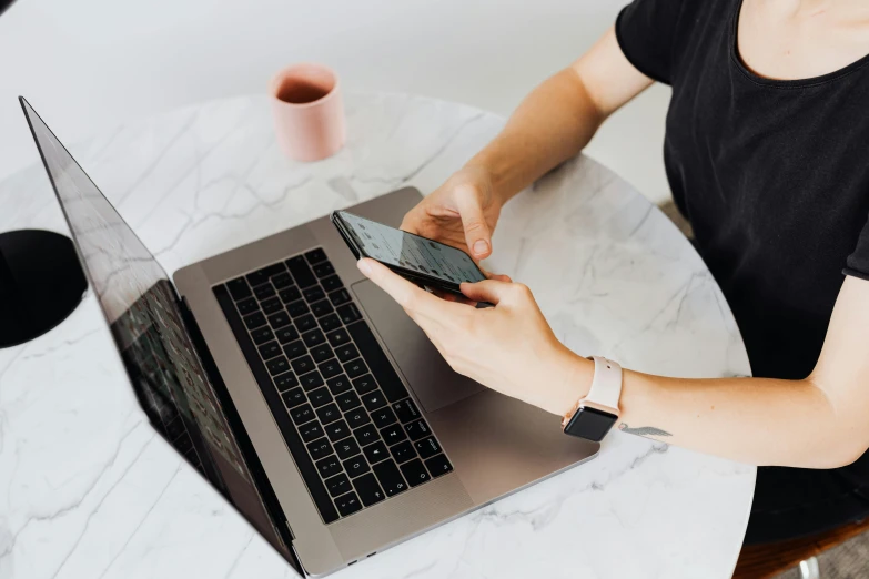 a woman sitting at a table with a laptop and cell phone, by Carey Morris, trending on pexels, marble table, creative coder with a computer, thumbnail, rectangle