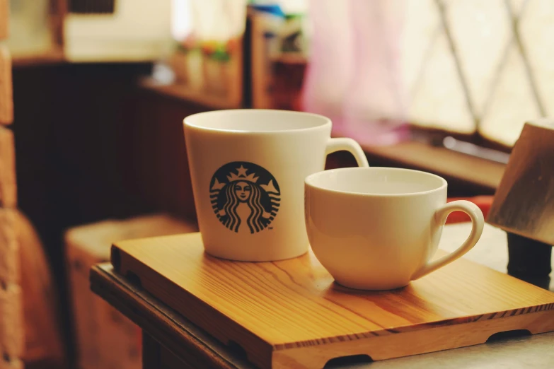 a couple of coffee cups sitting on top of a wooden table, a photo, unsplash, renaissance, illustrated starbucks interior, square, leaked image, is ((drinking a cup of tea))