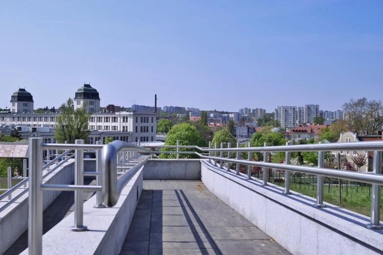 a view of a city from the top of a building, bauhaus, railing along the canal, bright sky, green terrace, from the side