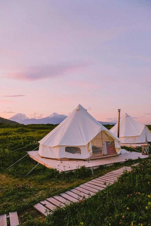 a group of tents sitting on top of a lush green field, pink skies, wooden platforms, alaska, rooftop romantic