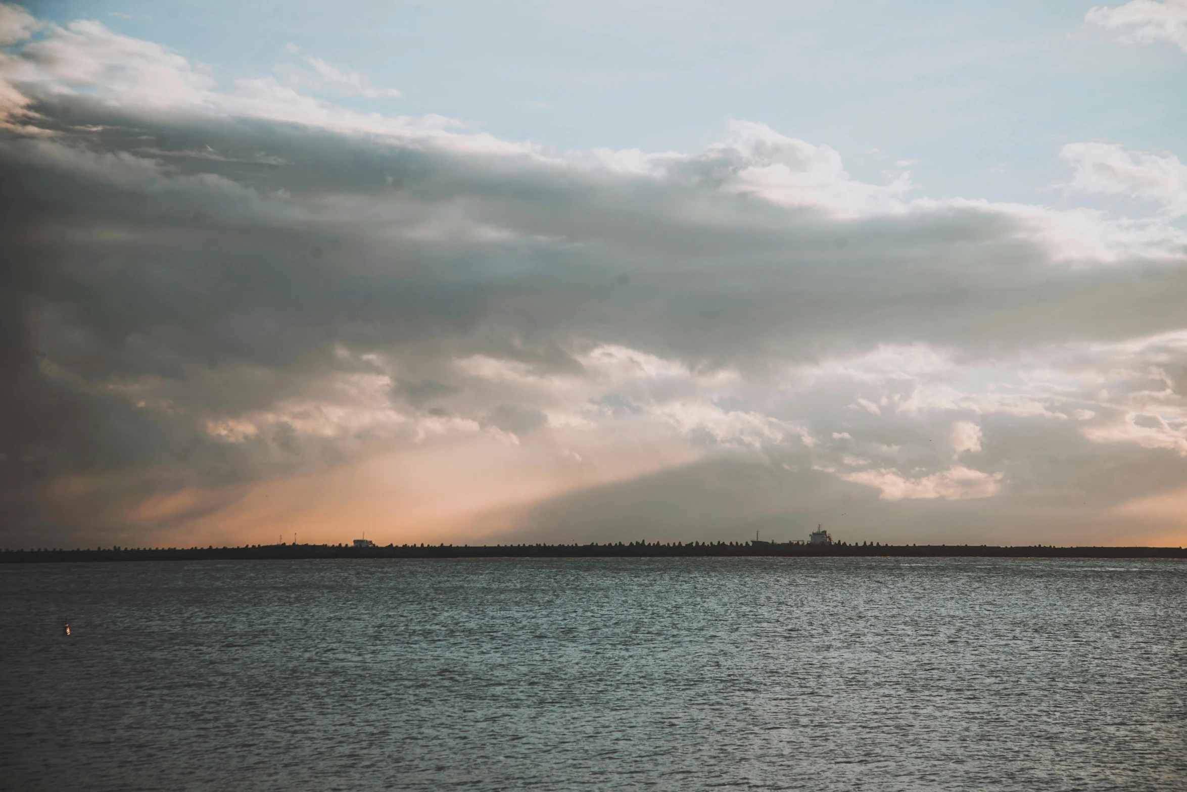 a sky view of sun shining through clouds over water