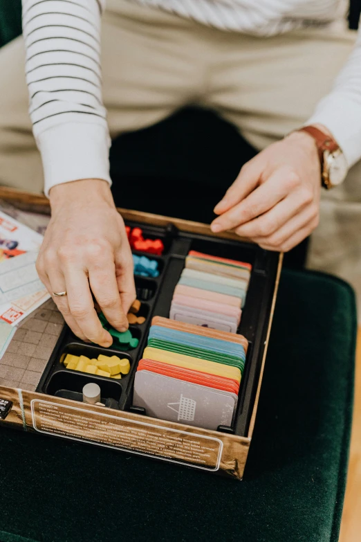 a person sitting on a chair with a box of colored pencils, a colorized photo, by Daniel Lieske, pexels contest winner, color field, playing board games, in suitcase, game icon, flatlay