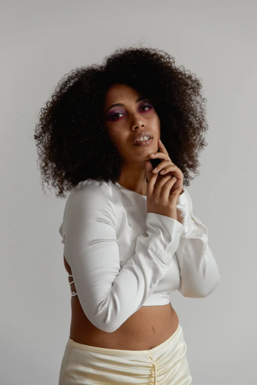 a woman holding a cell phone to her ear, an album cover, inspired by Esaias Boursse, trending on pexels, curls and curves, white outfit, beautiful midriff, looking towards camera