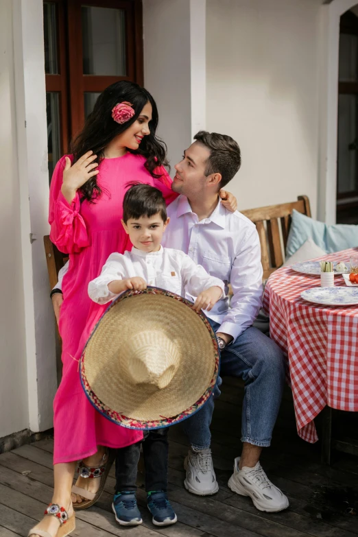 a man sitting on a bench next to a woman and a boy, sombrero, wearing a pink dress, family dinner, photoshoot