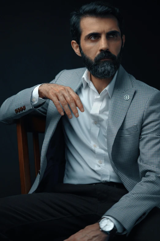 a man with a beard in a suit is sitting in a chair