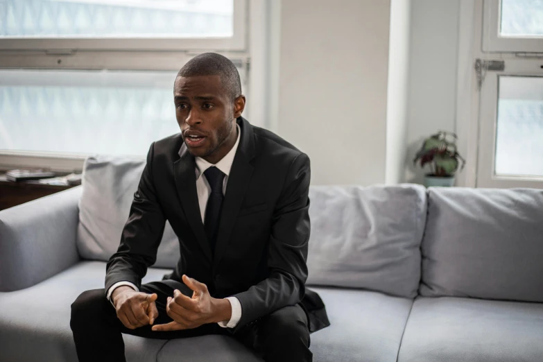 a man in a suit sitting on a couch talking to someone