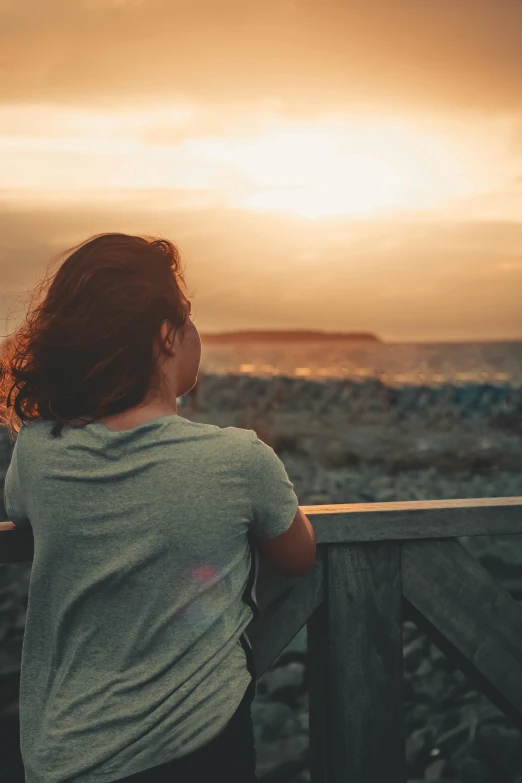 a woman standing on a wooden railing looking out over the ocean