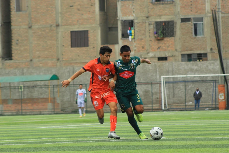 two young men playing soccer in front of a tall brick building