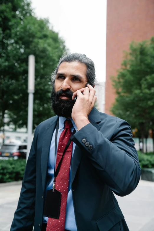 a man talking on a cell phone wearing a blue suit with red tie and black jacket