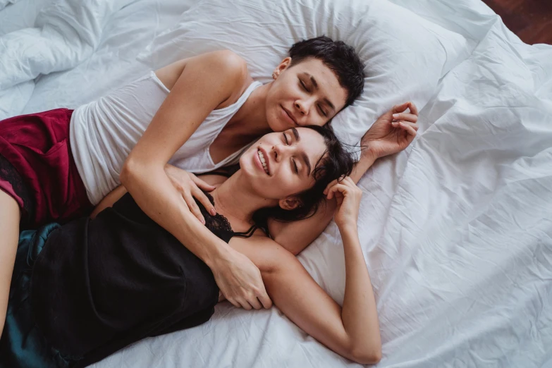 two women lay down on a white bed together