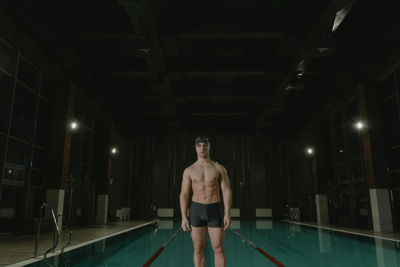 a shirtless man stands next to a pool in the middle of a room