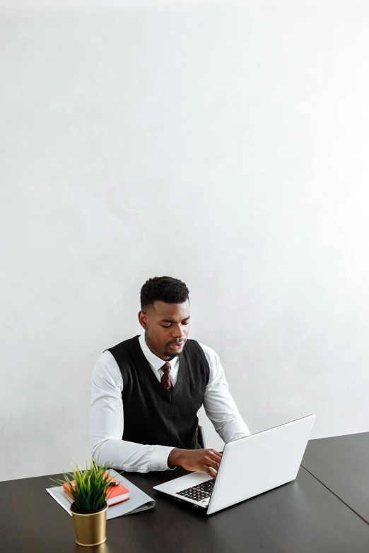 a man in a sweater vest working on a laptop
