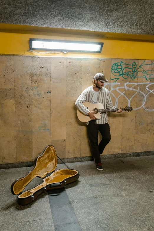 a man leaning against a wall while holding a guitar