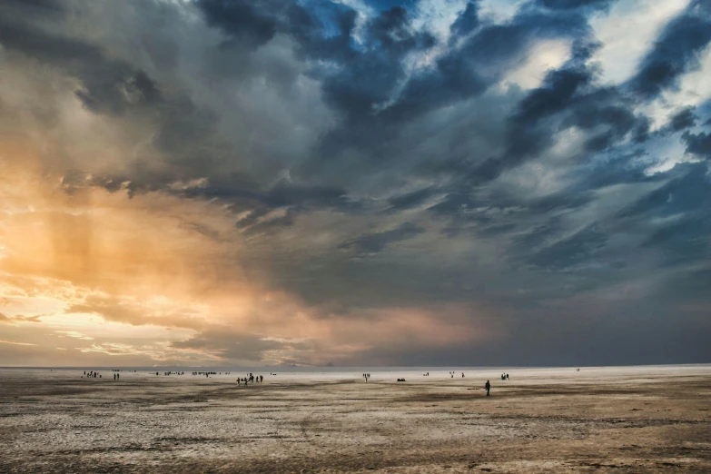 people are riding their horses on the beach in front of dark storm clouds