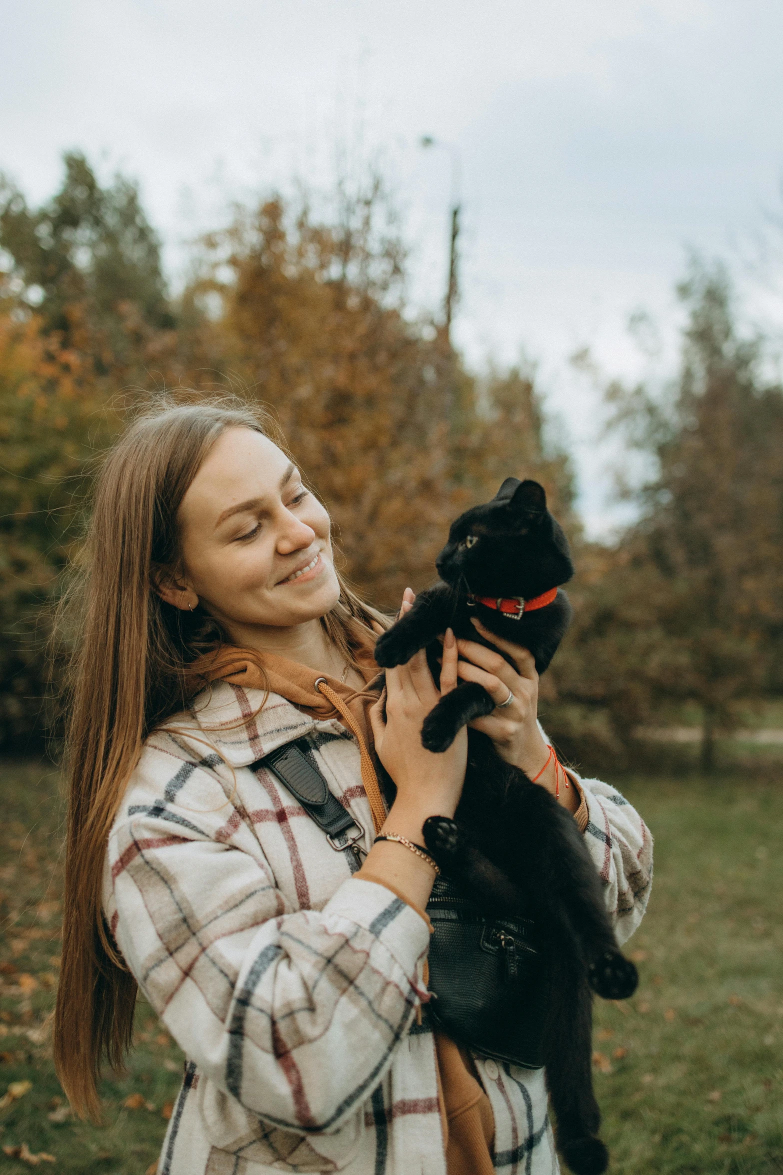 a woman holding a cat in her arms while she stands in the woods