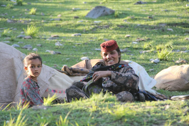 a woman and a child sitting on a green lawn with rocks in the background