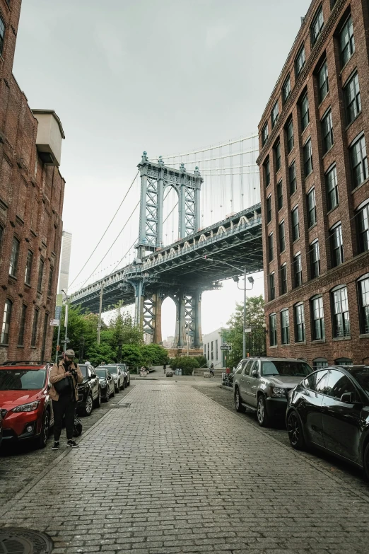 a brick street with cars parked along it and a bridge in the background