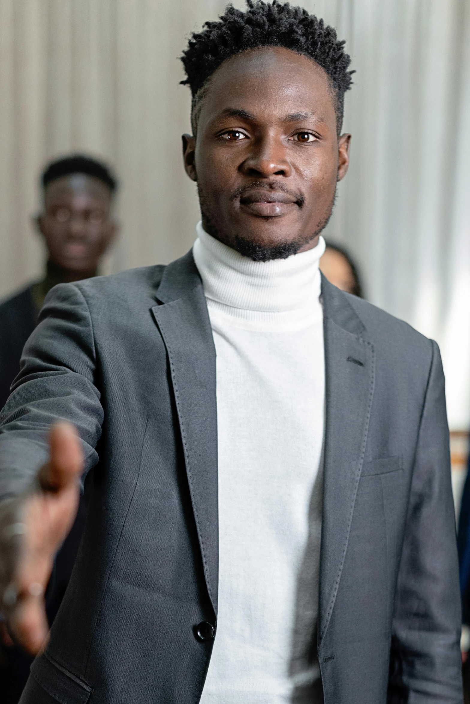 a man wearing a turtle neck, black suit and white sweater stands in front of people