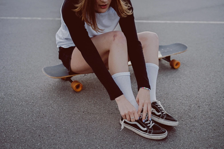 a girl sitting on her skateboard tying her shoes