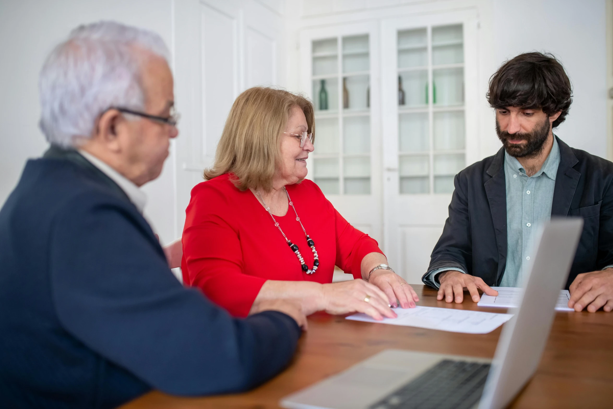 three people at a table with one man holding a notebook and the other woman signing documents