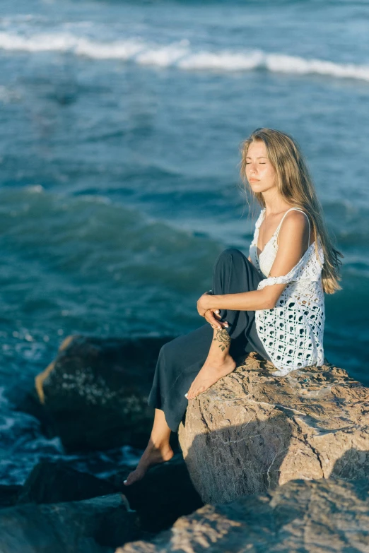 a beautiful young lady sitting on a rock over looking the ocean
