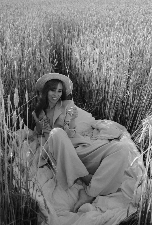 a woman wearing a hat laying in a field with long grass