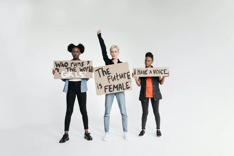 three people stand holding signs with writing on them