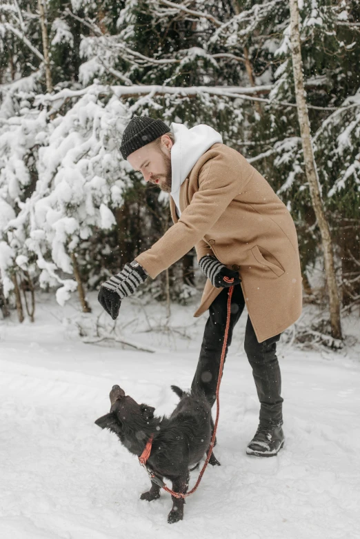 man in a jacket playing with a black dog