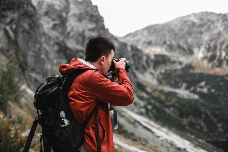 the man stands with a camera in his hands, overlooking the mountains