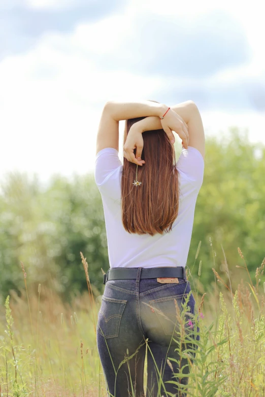 a woman holding her arms behind her head, standing in tall grass