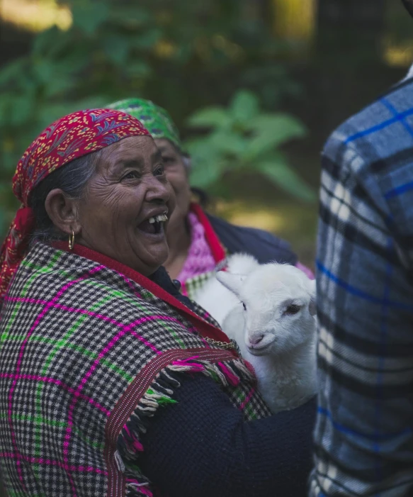 an old lady with a baby goat inside of her arms