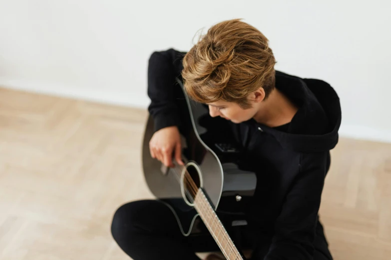 the young person is sitting on a wooden floor with her guitar