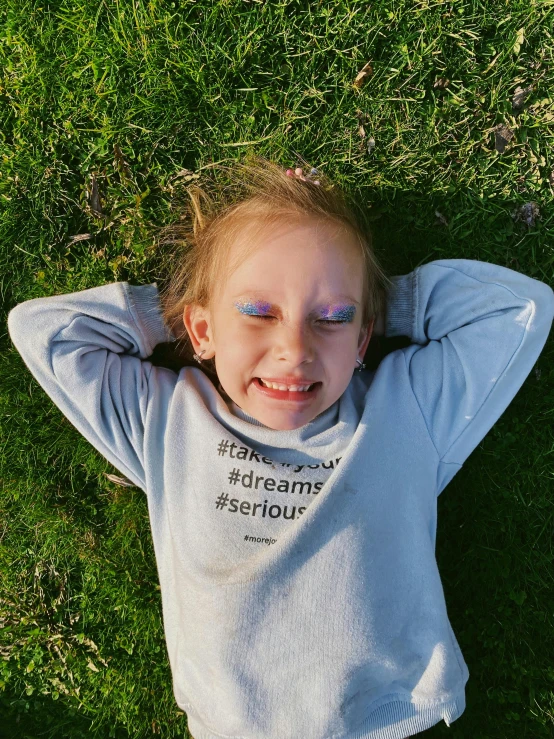 the child with colored eyes smiles while laying in the grass