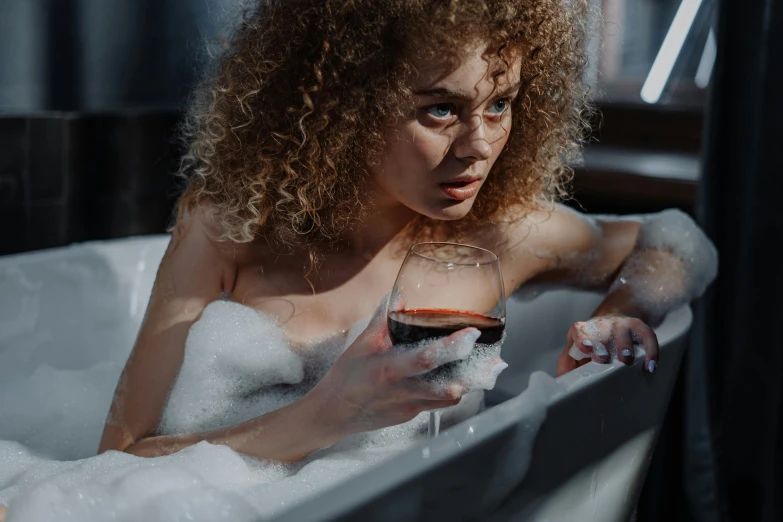 a woman sitting in a bubble bath with a glass of red wine