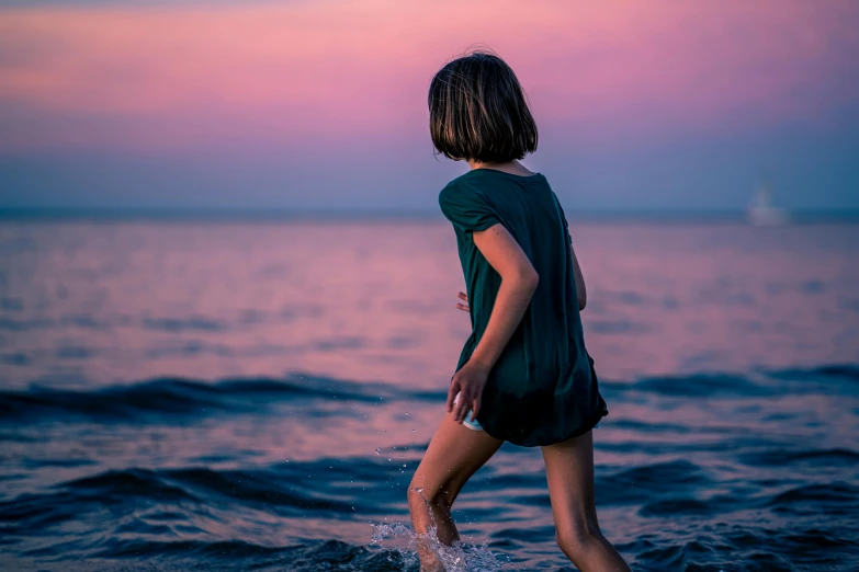 a young person standing in the ocean at sunset