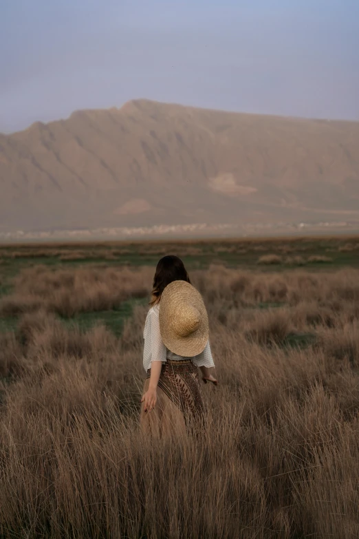 a woman walking through tall grass towards a mountain