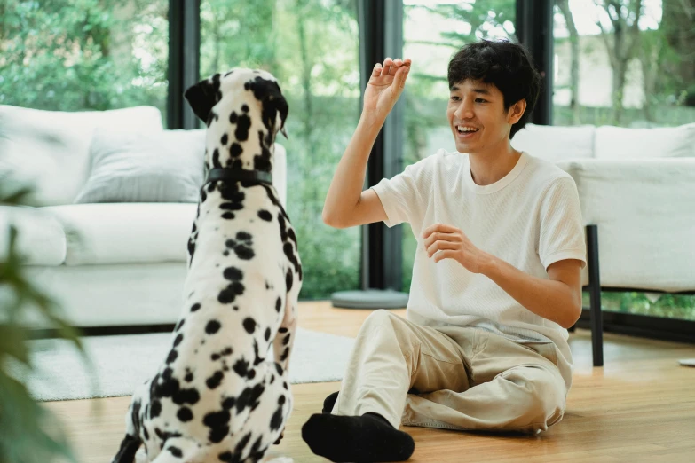 a man sitting on the floor next to a dalmatian dog and waving to his right