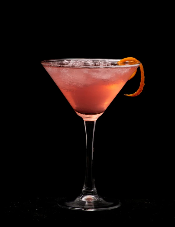 a pink cocktail served in a goblet with a half an orange peel