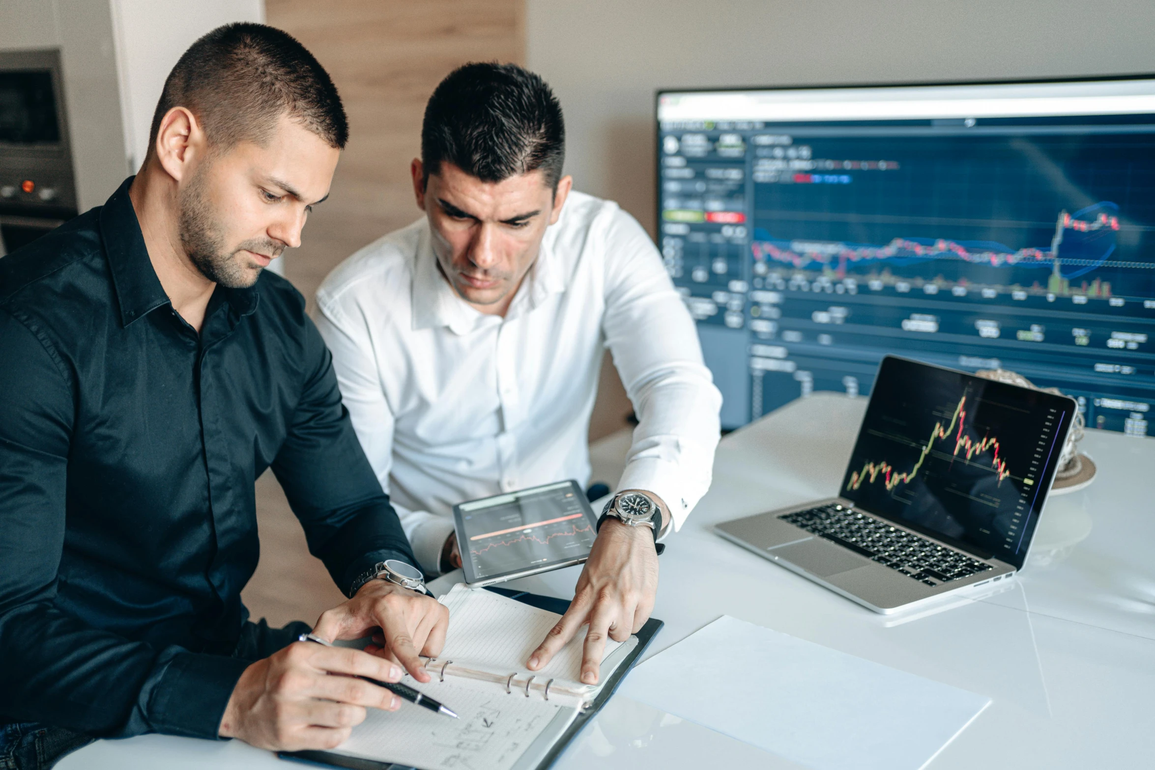 two men looking at paperwork in front of computers