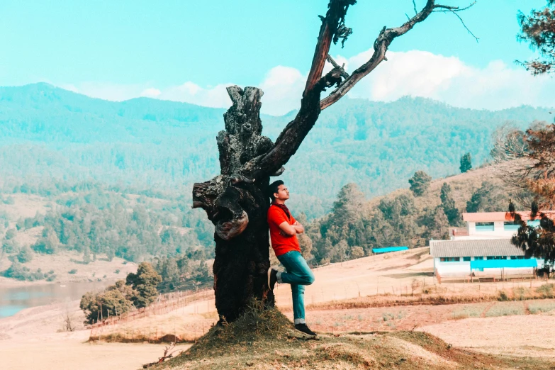 a man standing next to a tree on top of a hill