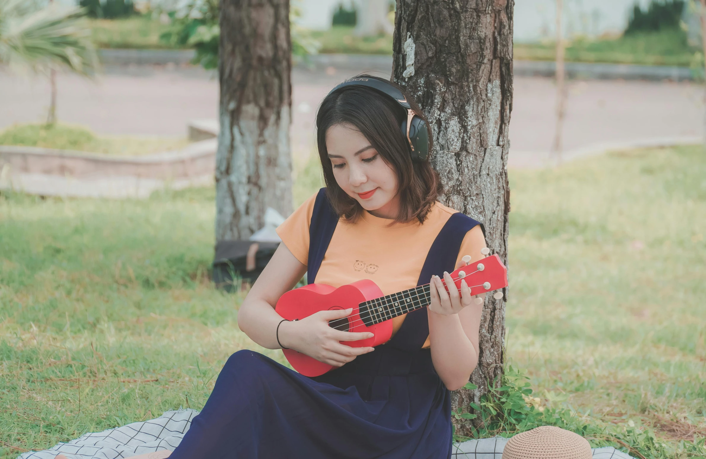 a girl holding a guitar sitting underneath a tree