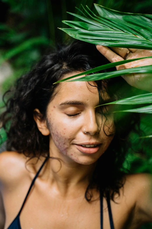 a woman standing behind some green leaves