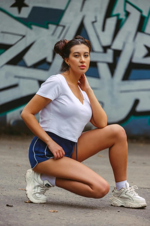 a young woman squats and poses next to a graffiti wall