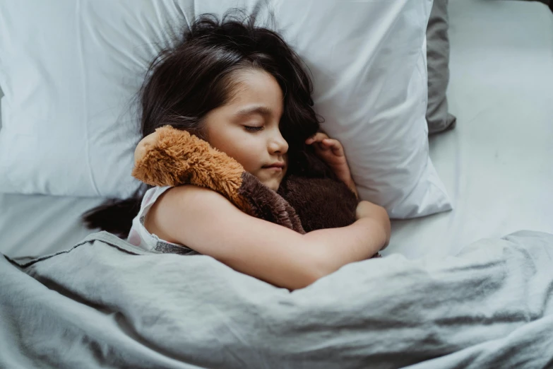 little girl sleeping on a bed with her teddy bear