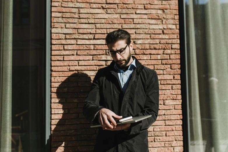 a man holding a smart phone standing against a brick wall