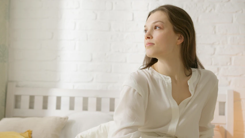 a woman sits on a bed and stares to the left