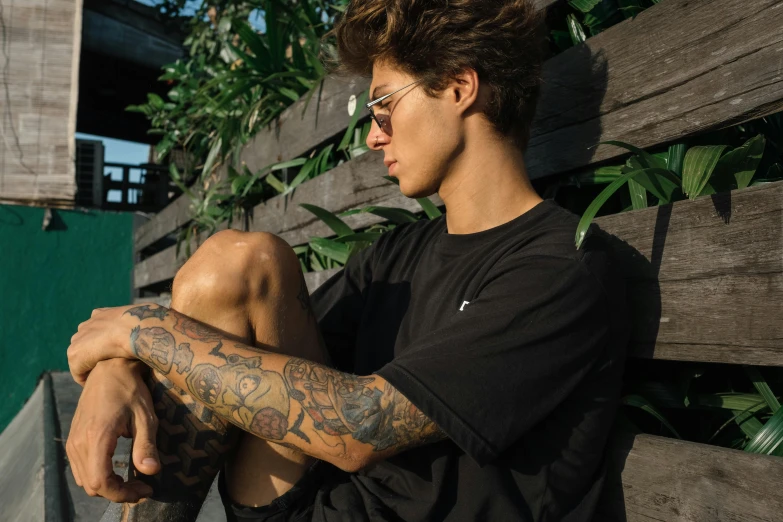 a young man sitting on top of a bench next to a wooden fence