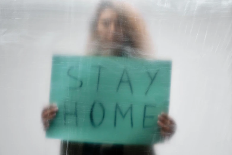 woman holding green sign reading stay home in reflection